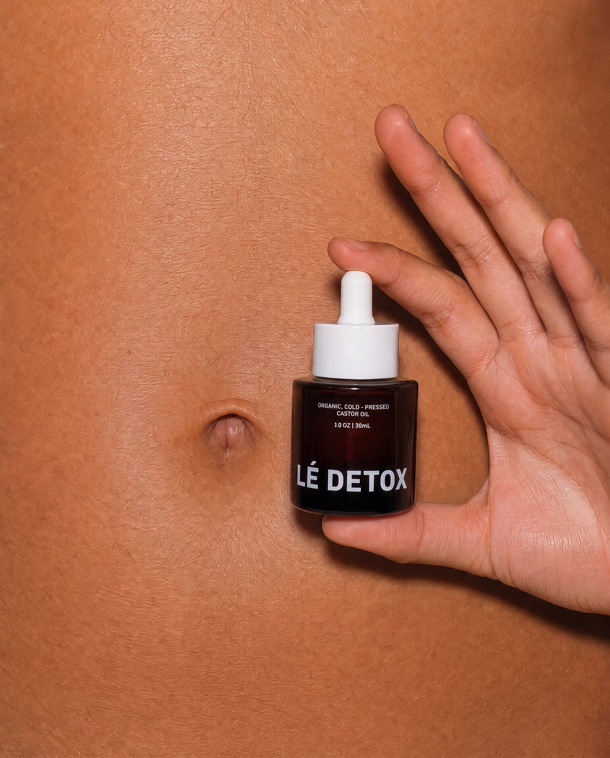 NAVELÉ bottle held against the abdomen during a personal wellness ritual.